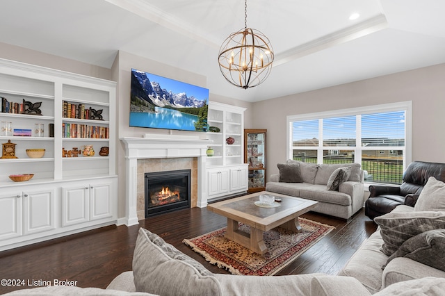 living room with ornamental molding, a tray ceiling, dark wood-type flooring, a notable chandelier, and a fireplace