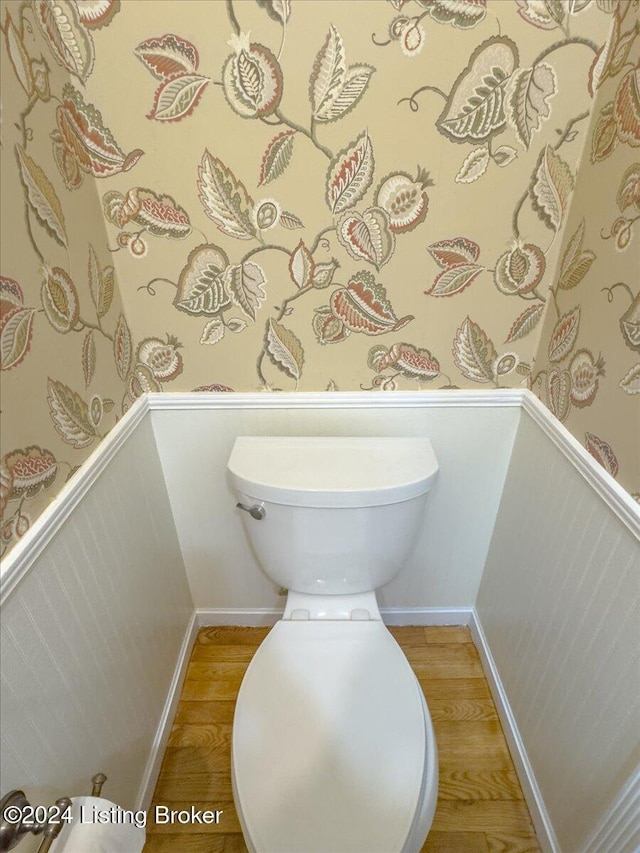 bathroom with wainscoting, wallpapered walls, and wood finished floors