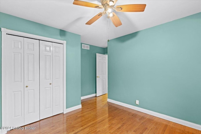 unfurnished bedroom with a closet, visible vents, a ceiling fan, wood finished floors, and baseboards