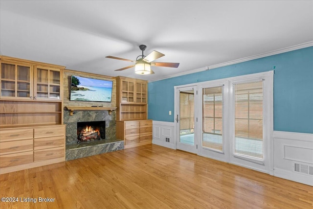 unfurnished living room featuring light wood finished floors, ornamental molding, a premium fireplace, and wainscoting