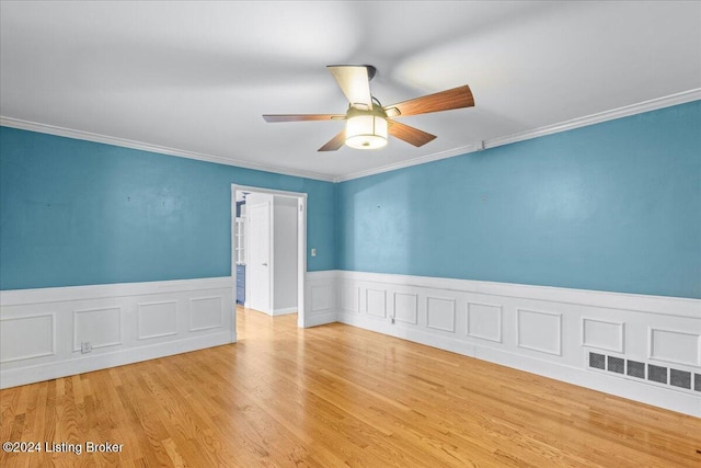 empty room featuring visible vents, a wainscoted wall, ceiling fan, wood finished floors, and crown molding