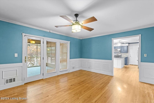 spare room with crown molding, light wood finished floors, visible vents, wainscoting, and ceiling fan