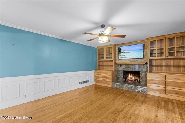 unfurnished living room featuring a ceiling fan, a fireplace, ornamental molding, and wood finished floors