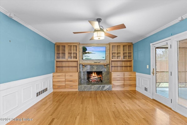 unfurnished living room with ceiling fan, a large fireplace, a wainscoted wall, wood finished floors, and crown molding