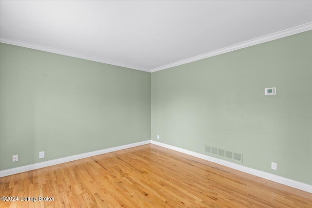 empty room with ornamental molding, wood finished floors, visible vents, and baseboards