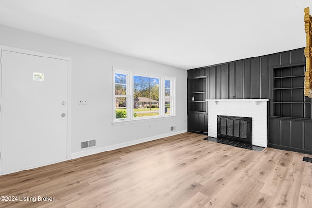 unfurnished living room with a fireplace, light wood-type flooring, and built in features