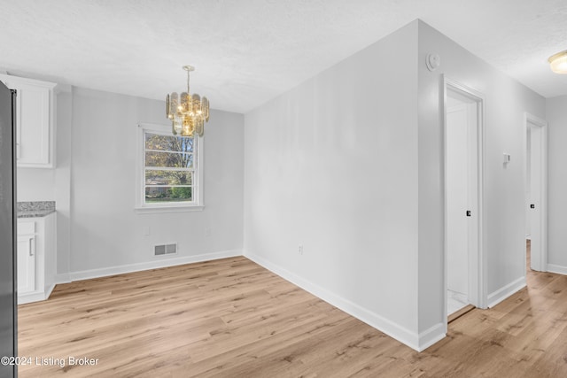 unfurnished dining area with a textured ceiling, a notable chandelier, and light wood-type flooring