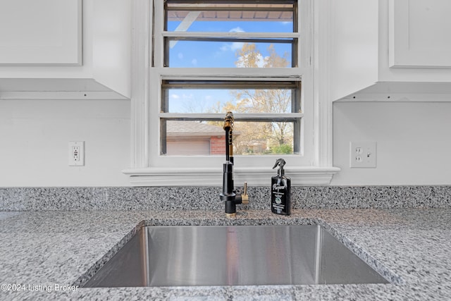 interior details featuring light stone counters, white cabinetry, and sink