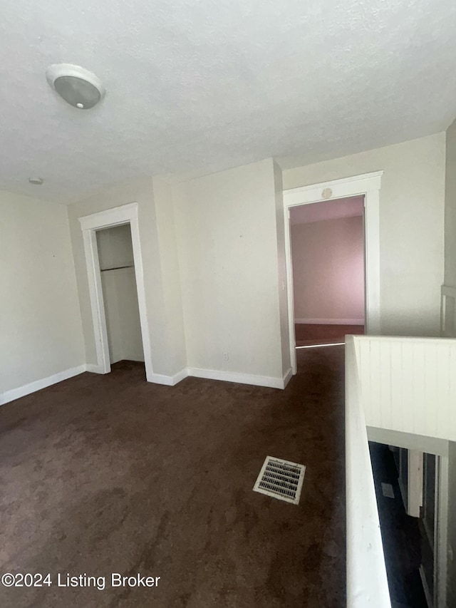 spare room featuring a textured ceiling and dark carpet