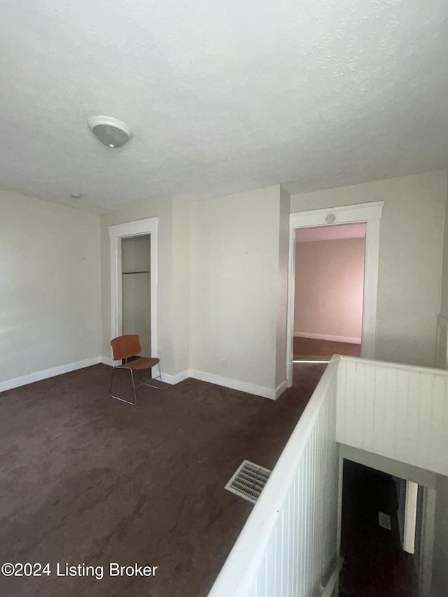 hall with dark colored carpet and a textured ceiling