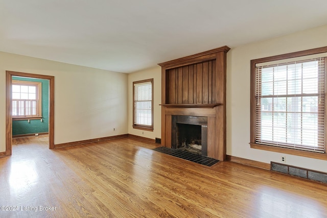 unfurnished living room featuring a fireplace, light hardwood / wood-style floors, and a healthy amount of sunlight