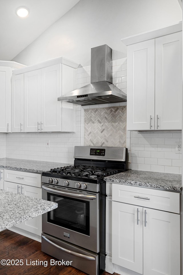 kitchen with vaulted ceiling, white cabinetry, stainless steel gas range oven, light stone countertops, and wall chimney range hood