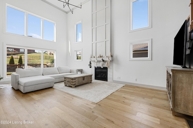 living room with a notable chandelier, crown molding, a high ceiling, and light hardwood / wood-style flooring