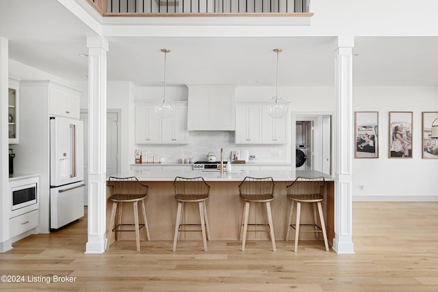 kitchen with light wood-type flooring, hanging light fixtures, appliances with stainless steel finishes, and decorative columns