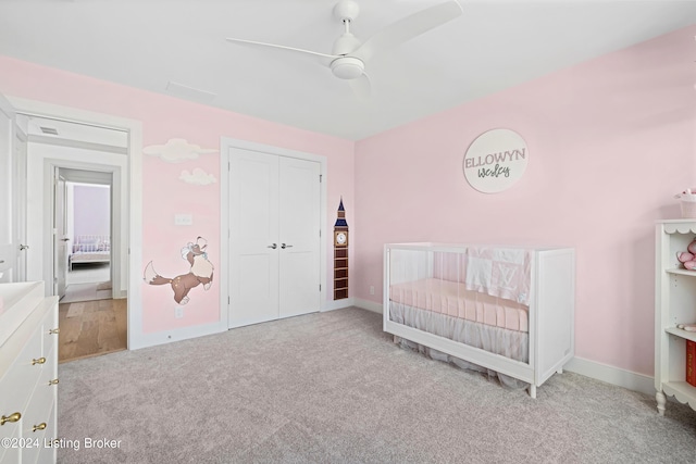 carpeted bedroom featuring ceiling fan and a nursery area