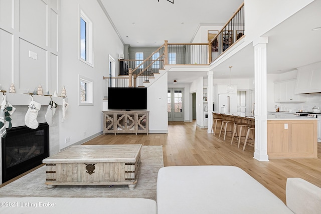 living room featuring a towering ceiling, light hardwood / wood-style floors, and decorative columns