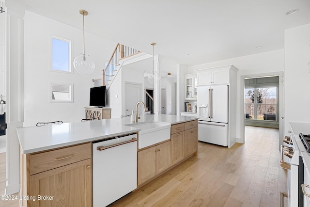 kitchen with high end appliances, hanging light fixtures, sink, light brown cabinetry, and light hardwood / wood-style floors