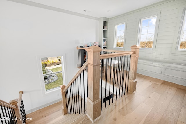 stairs featuring wood-type flooring, ornamental molding, and a healthy amount of sunlight