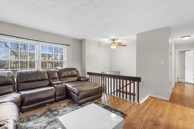 living room with ceiling fan, light wood-type flooring, and a textured ceiling