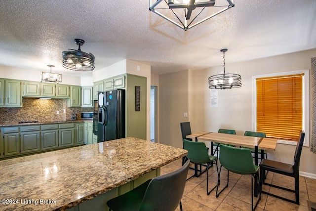 kitchen featuring a textured ceiling, green cabinets, black fridge with ice dispenser, and light stone counters