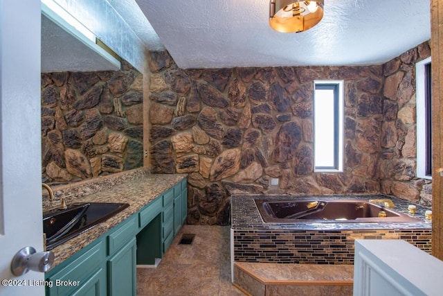 bathroom with vanity, tile patterned flooring, a relaxing tiled tub, and a textured ceiling