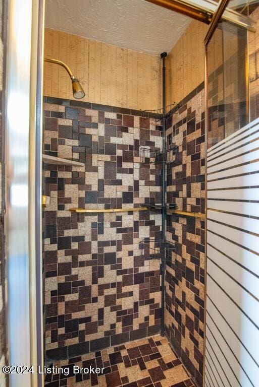 bathroom featuring a tile shower, a textured ceiling, and wooden walls