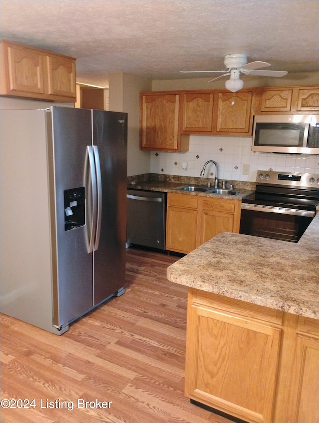 kitchen featuring sink, stainless steel appliances, light hardwood / wood-style flooring, a textured ceiling, and decorative backsplash