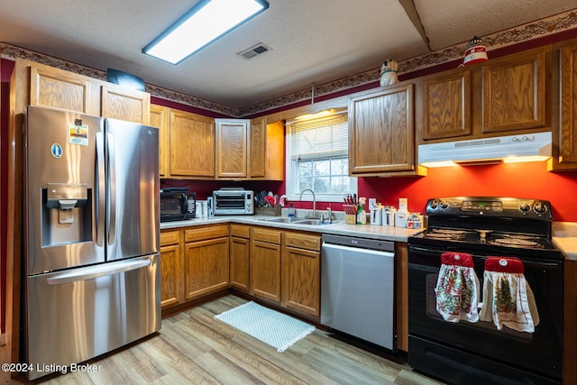 kitchen featuring appliances with stainless steel finishes, a textured ceiling, light hardwood / wood-style flooring, and sink