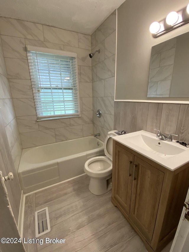 full bathroom featuring toilet, tile walls, vanity, tiled shower / bath combo, and hardwood / wood-style floors