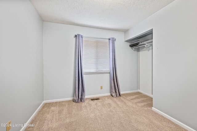 unfurnished bedroom featuring a textured ceiling, light colored carpet, and a closet