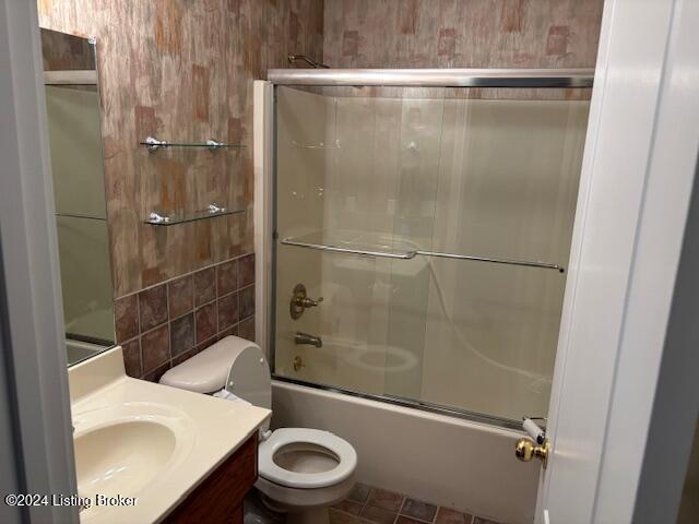 full bathroom with combined bath / shower with glass door, vanity, toilet, and tile patterned flooring