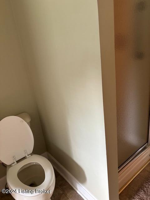 bathroom featuring tile patterned floors, toilet, and a shower with door