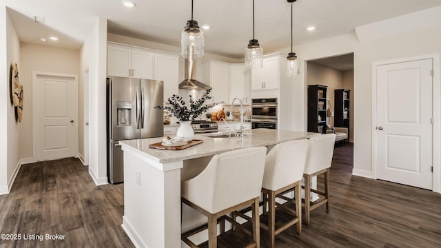 kitchen featuring decorative light fixtures, white cabinets, appliances with stainless steel finishes, and an island with sink