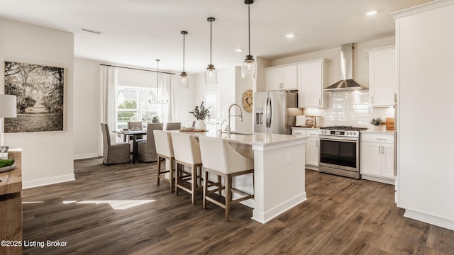 kitchen featuring wall chimney exhaust hood, pendant lighting, a kitchen island with sink, white cabinetry, and appliances with stainless steel finishes