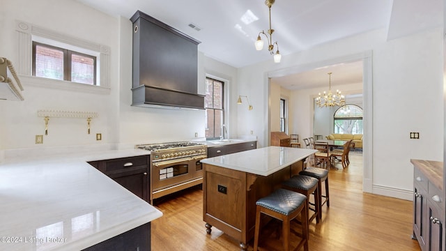 kitchen featuring a chandelier, pendant lighting, range with two ovens, light hardwood / wood-style floors, and custom range hood