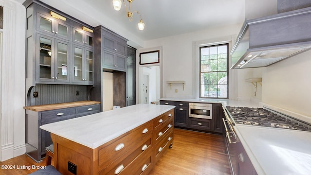 kitchen with wall chimney range hood, decorative light fixtures, and hardwood / wood-style flooring