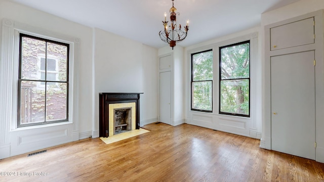 unfurnished living room with light wood-type flooring, an inviting chandelier, and plenty of natural light