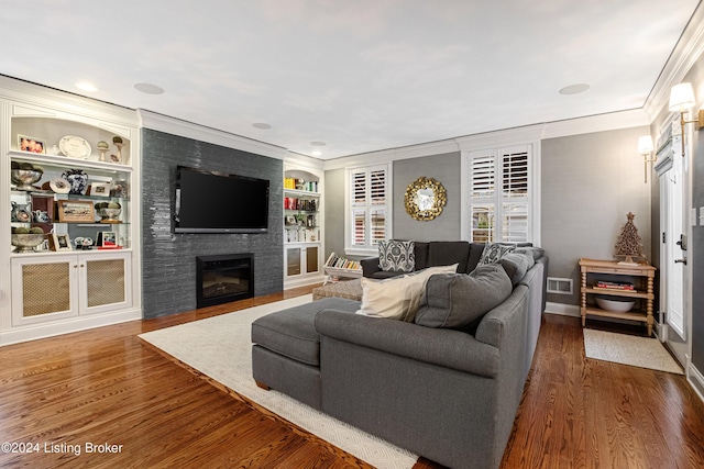 living room with dark hardwood / wood-style flooring, built in features, crown molding, and a fireplace