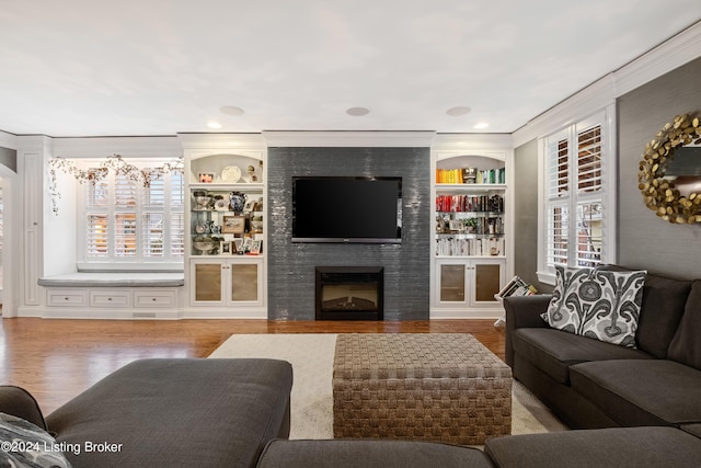 living room with ornamental molding, a fireplace, hardwood / wood-style floors, and built in features