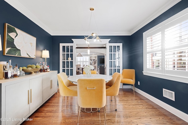 dining space featuring bar area, light wood-type flooring, french doors, and ornamental molding