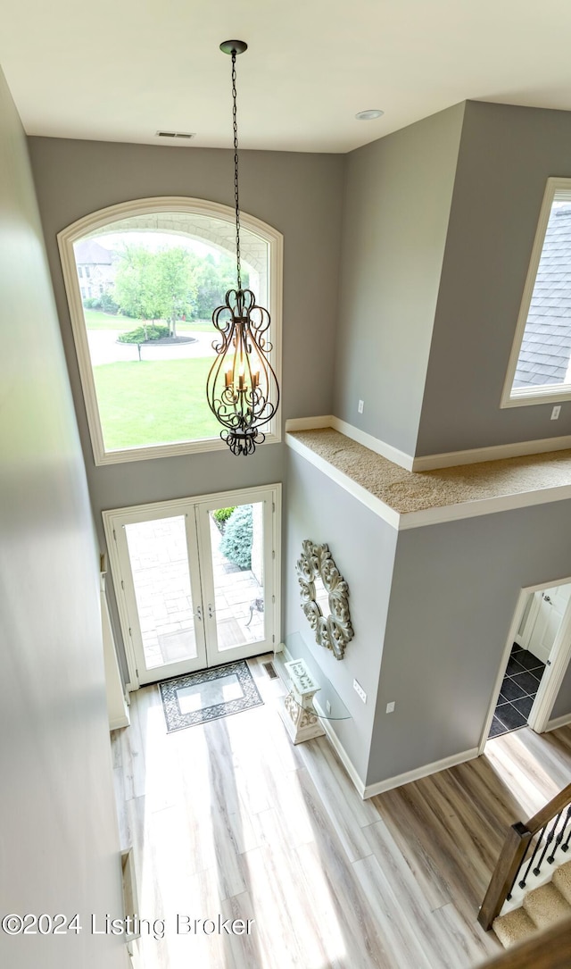 foyer entrance with plenty of natural light, an inviting chandelier, french doors, and light hardwood / wood-style flooring