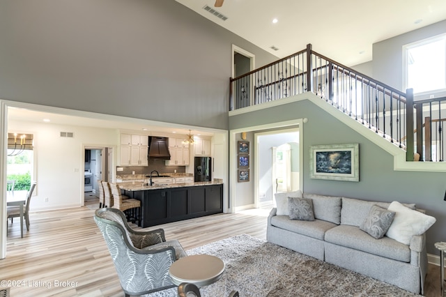 living room with sink, a healthy amount of sunlight, a high ceiling, and light hardwood / wood-style flooring