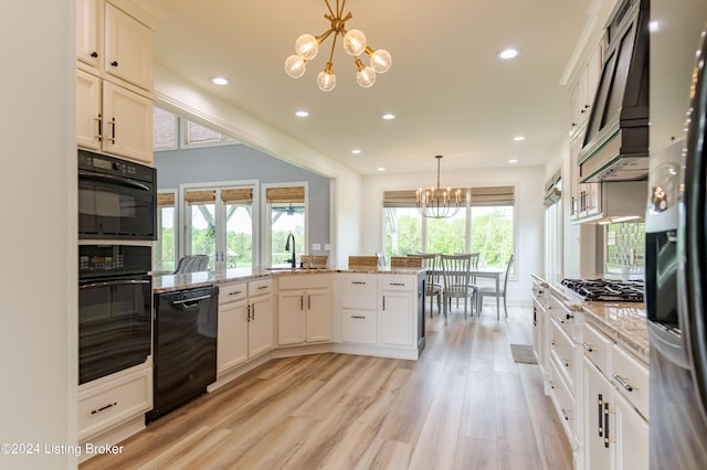 kitchen with light stone counters, hanging light fixtures, black appliances, and an inviting chandelier