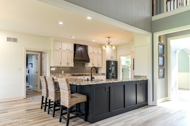 kitchen featuring custom exhaust hood, black fridge with ice dispenser, sink, light hardwood / wood-style flooring, and white cabinets