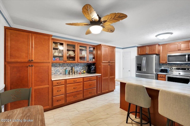 kitchen with stainless steel appliances, ornamental molding, ceiling fan, and decorative backsplash