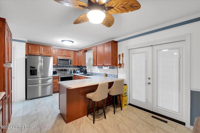 kitchen featuring sink, a breakfast bar area, ceiling fan, stainless steel appliances, and kitchen peninsula