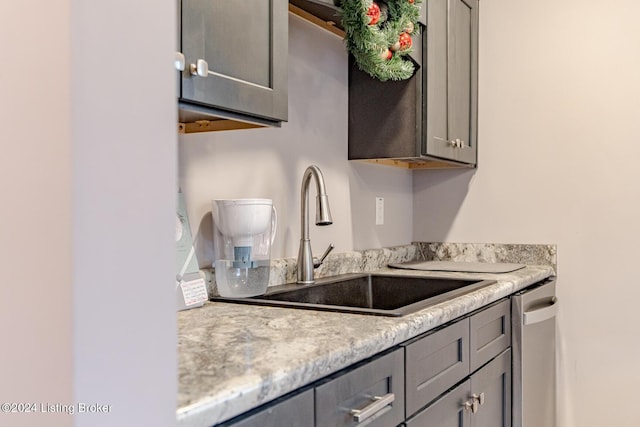 kitchen featuring gray cabinetry, light stone counters, stainless steel dishwasher, and sink