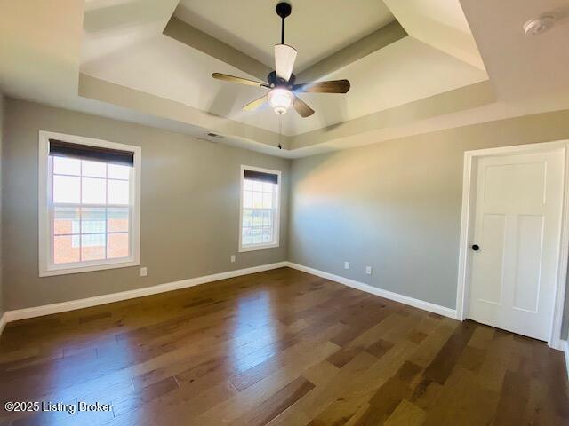 empty room with a tray ceiling, baseboards, a ceiling fan, and dark wood-style flooring