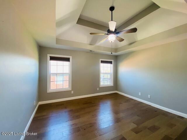 empty room with dark wood finished floors, a tray ceiling, baseboards, and ceiling fan