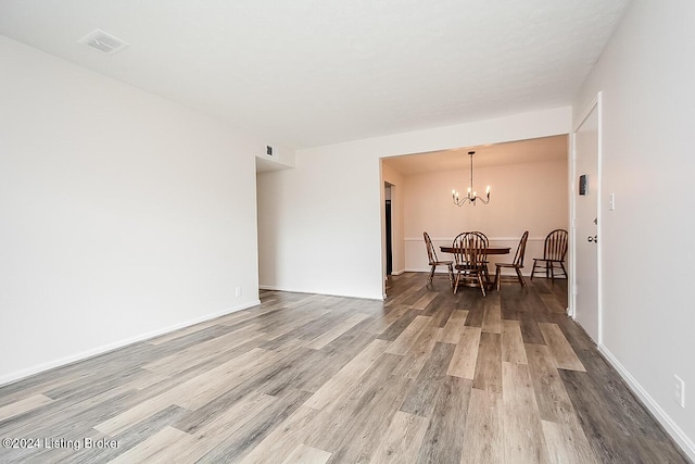 empty room with wood-type flooring and an inviting chandelier